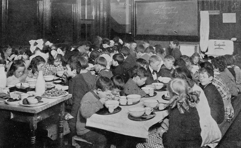 Children eating a school lunch at long tables, from a 1913 book on health and the school
